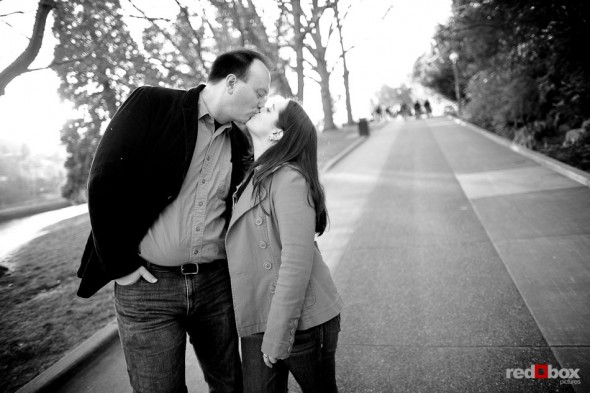 Tara and Brian kiss while walking at the Ballard Locks during their engagement session. (Photography by Andy Rogers/Red Box Pictures)