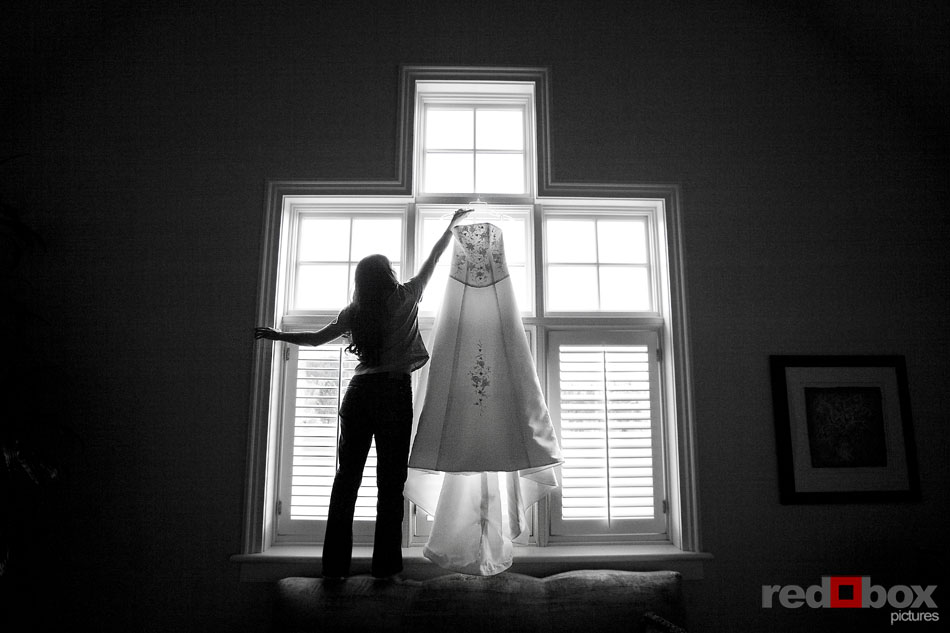 The bride grabs her wedding dress hanging by the window at the Golf Club at Newcastle outside Seattle. (Wedding Photography by Scott Eklund/Red Box Pictures)