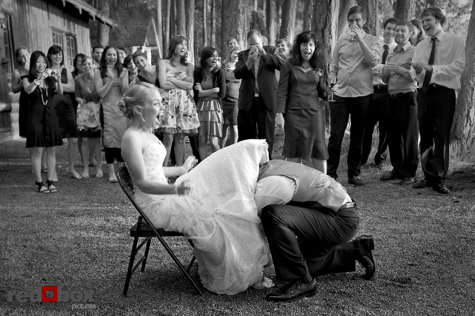 The groom takes the garter off the bride at the reception at their Kitsap Memorial State Park wedding in Poulsbo, WA. Seattle Wedding Photographers Red Box Pictures Scott Eklund