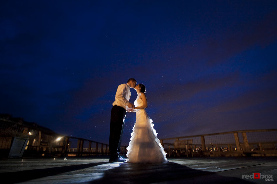 The bride and groom kiss on a dock at twilight at Semiahmoo Resort in Blaine, WA. Seattle Wedding Photographer Scott Eklund Red Box Pictures