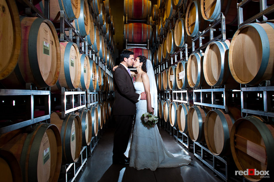 Laura and Nathan steal a kiss among the wine barrels during their wedding reception at the Novelty Hill Januik Winery in Woodinville, WA. (Photo by Dan DeLong/Red Box Pictures)