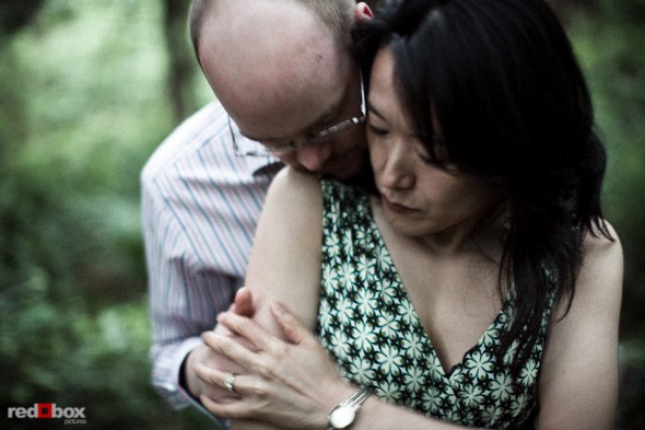 Nobuyo and Rory embrace among the trees in Seward Park during their engagement portrait session in Seattle. (Photography by Andy Rogers/Red Box Pictures)