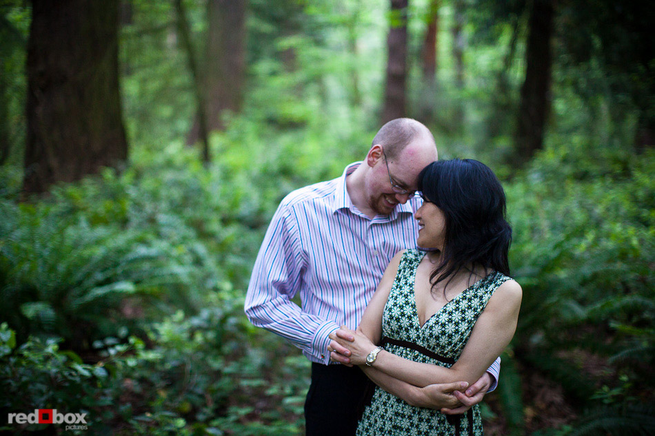 Nobuyo and Rory embrace among the trees during their engagement portrait session at Seward Park in Seattle. (Photography by Andy Rogers/Red Box Pictures)
