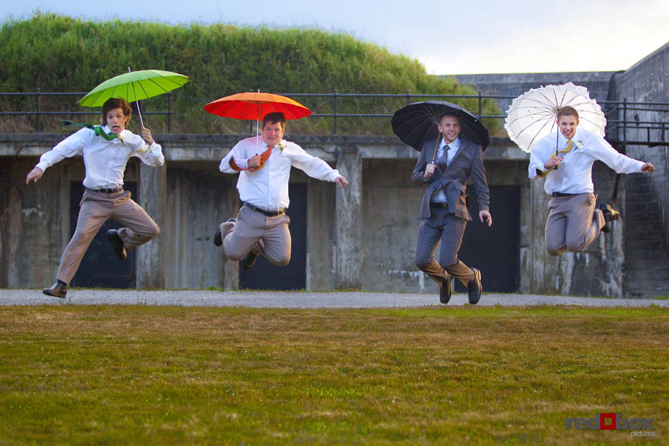 The groom and his groomsmen try and catch a little air as they go airborne with their umbrellas at Fort Casey State Park on Whidbey Island. (Seattle Wedding Photography by Scott Eklund Red Box Pictures)