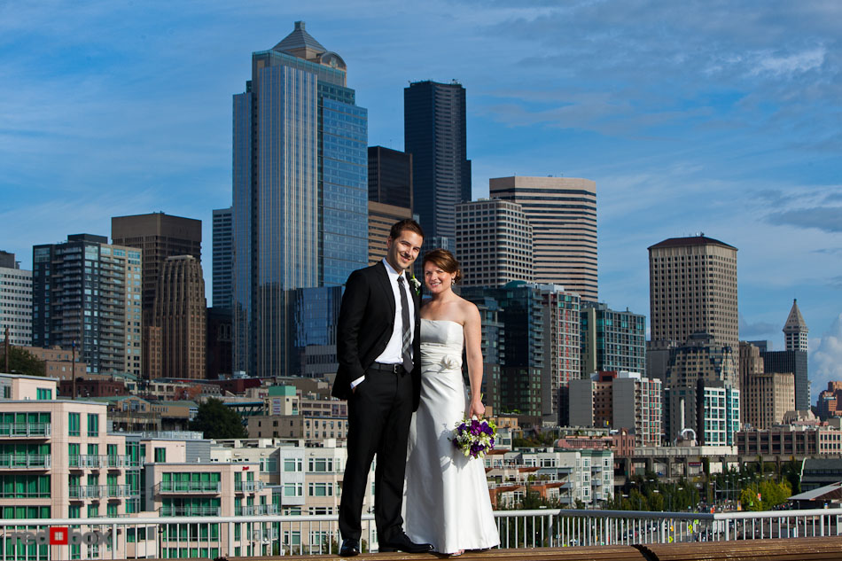 Lisa and Alex stand on the Bell Street Pier in front of the Seattle skyline prior to their wedding at the Edgewater Hotel. (Photo by Andy Rogers/Red Box Pictures)
