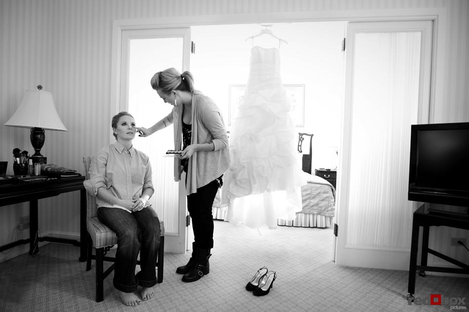 The bride gets her makeup touched up as her wedding dress hangs nearby at the Fairmont Olympic Hotel in Seattle, before her wedding at the Top of the Market at the Pike Place Market in Seattle. (Wedding Photographer Scott Eklund/Red Box Pictures/Seattle)