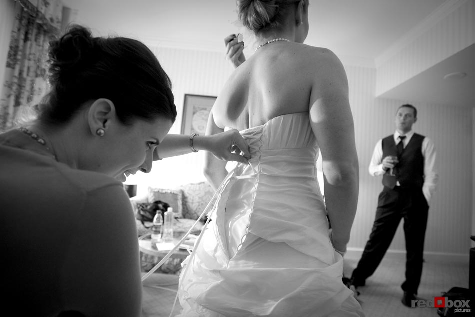 The maid of honor laces up the corset on the wedding dress as the bride gets ready at the Fairmont Olympic Hotel in Seattle, before the wedding at the Top of the Market at the Pike Place Market in Seattle. Wedding Photographer Scott Eklund/Red Box Pictures-Seattle