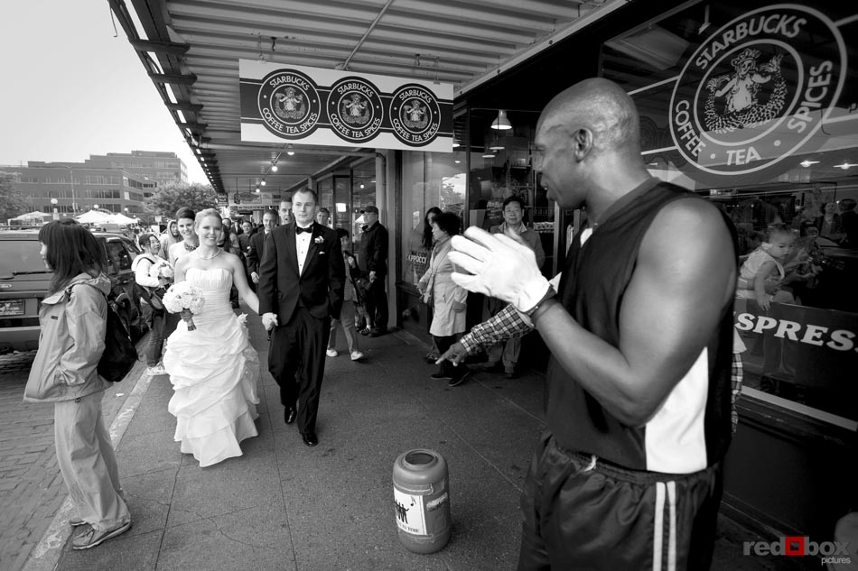 The bride & groom and wedding party walk through the Pike Place Market in Seattle, past the original Starbucks, on their way to their wedding at the Top of the Market. Seattle Wedding Photographer-Scott Eklund-Red Box Pictures