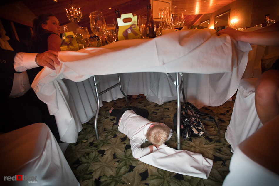 A young guest crashes under a table during the wedding reception at the Edgewater Hotel. (Photo by Andy Rogers/Red Box Pictures)