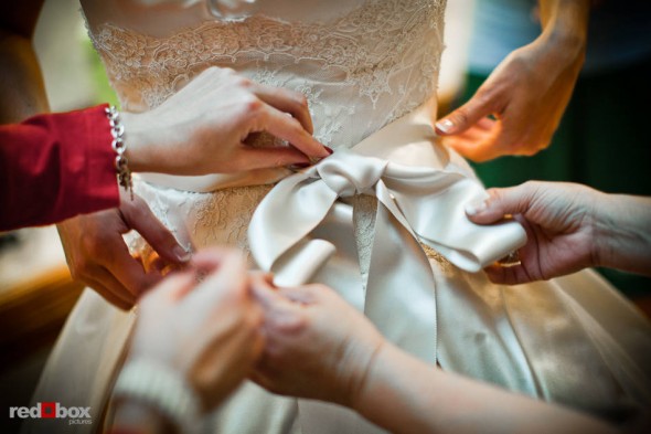 Bridesmaids help Suzy tie the bow of her wedding dress before she and Michael are married at Kiana Lodge in Poulsbo, WA. (Photo by Dan DeLong/Red Box Pictures)