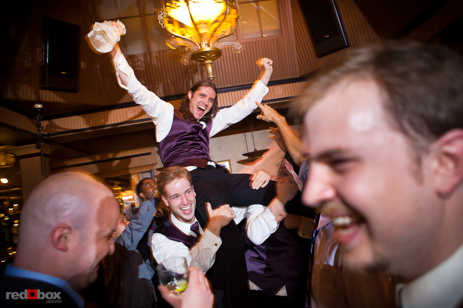 A guest celebrates the catching of the garter while being lifted on the shoulders of other guests during the wedding reception at the Lake Union Cafe in Seattle. (Photography by Andy Rogers/Red Box Pictures)