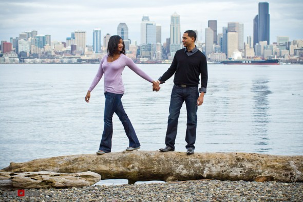 Nick and Tia walk on a large piece of driftwood at Seacrest Park in West Seattle for their engagement photo. (Photography by Andy Rogers/Red Box Pictures)