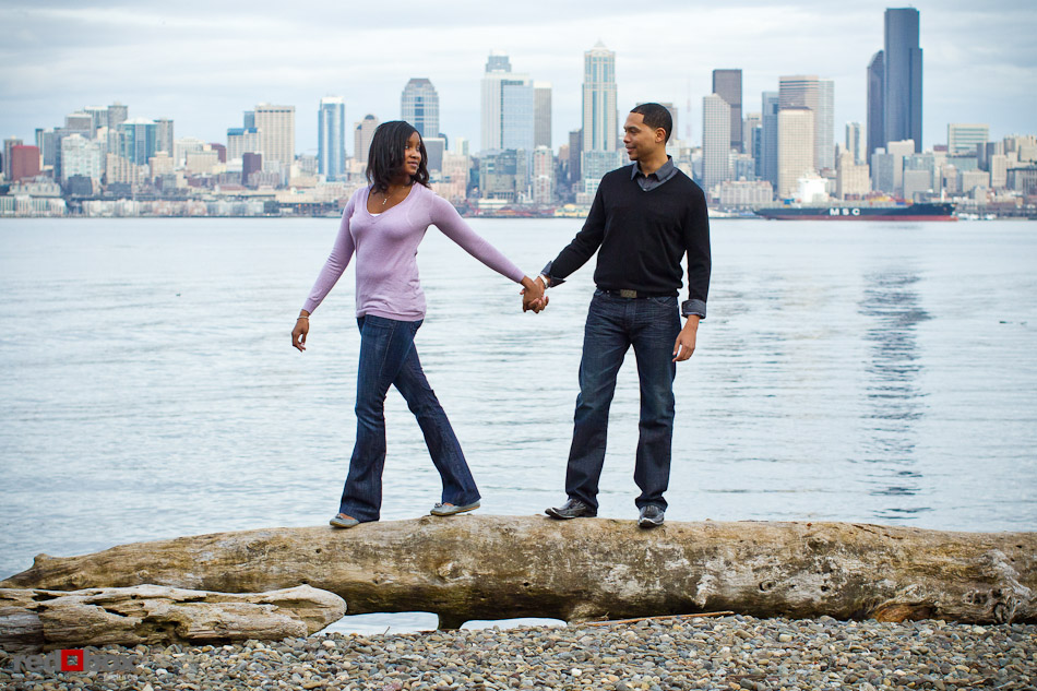 Nick and Tia walk on a large piece of driftwood at Seacrest Park in West Seattle for their engagement photo. (Photography by Andy Rogers/Red Box Pictures)