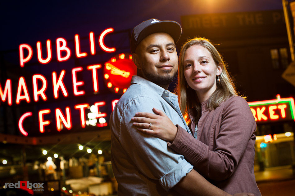 Carlos and Megan pose outside the Pike Place Market's famous sign and clock during engagement photography session in Seattle. (Photo by Dan DeLong/Red Box Pictures)