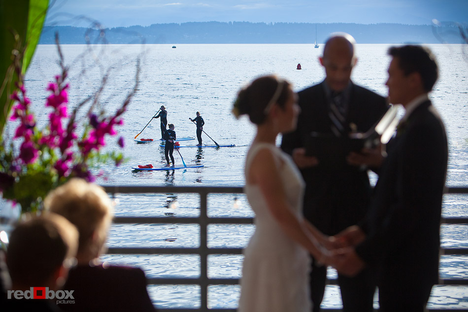 Paddleboarders pass Ray's Cafe during Laura and Ted's wedding ceremony on the deck of the Northwest Room at Ray's Boathouse in Seattle. (Photo by Andy Rogers/Red Box Pictures)