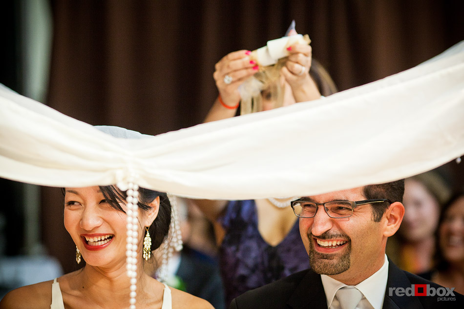 Two sugar cones or "Kalleh Ghand" are ground above a silk scarf over Jane and Kia's heads as they sit in front of the Sofreh during the Persian wedding ceremony at Velocity Dance Center in Seattle. (Photo by Andy Rogers/Red Box Pictures)