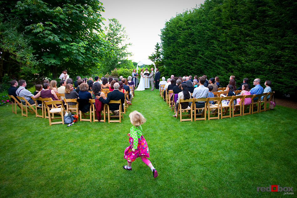 A little girl runs around the guests as the bride and groom exchange their vows during their ceremony at The Hall at Fauntleroy in West Seattle, WA. (Seattle Wedding Photographer Scott Eklund/Red Box Pictures)