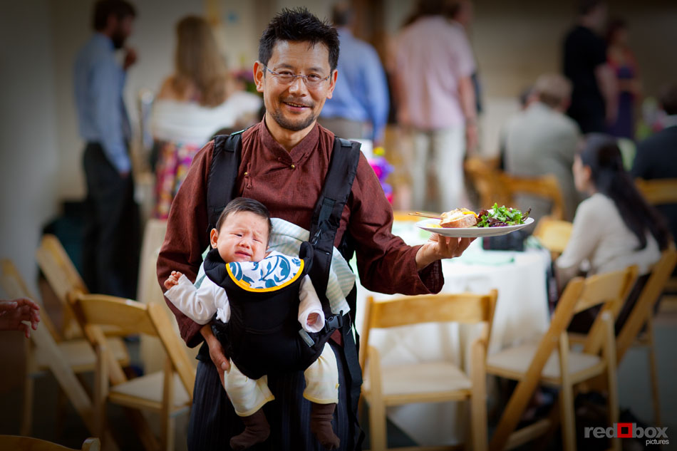 A guest juggles some of the delicious food prepared by Tuxedos and Tennis Shoes and his baby at the reception of Anna & Tommy at The Hall at Fauntleroy in West Seattle, WA. (Seattle Wedding Photographer Scott Eklund/Red Box Pictures)