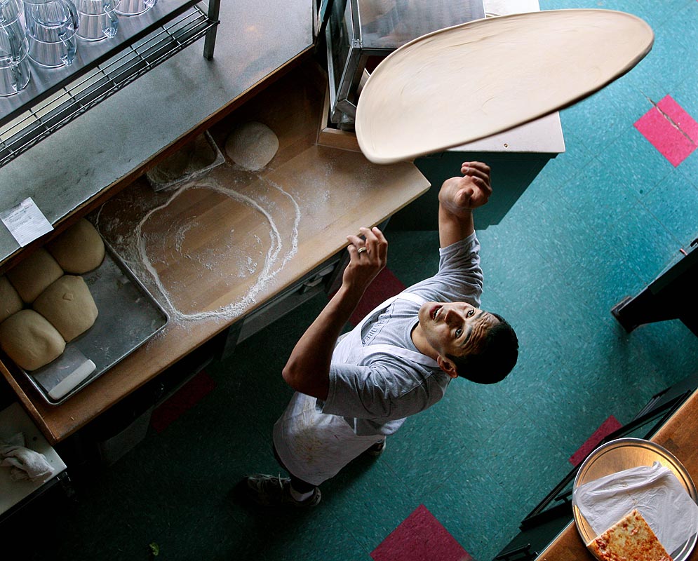 Roberto Aguilar tosses a pizza for diners at Piecora's New York Pizza on Capitol Hill in Seattle. (Photographer: Dan DeLong)
