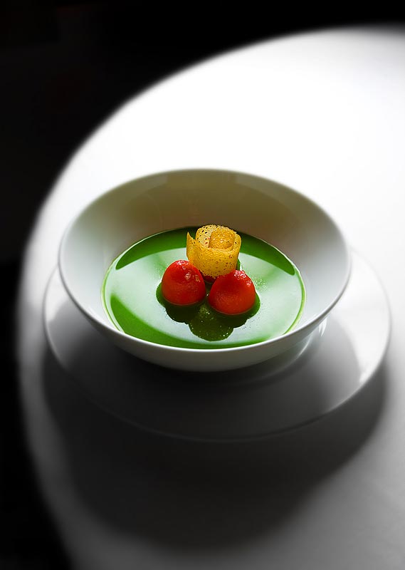 Peeled cherry tomatoes filled with black cod puree in a chilled spring vegetable consomme and an orange tuile at Lampreia Restaurant in Seattle (Photographer: Scott Eklund)